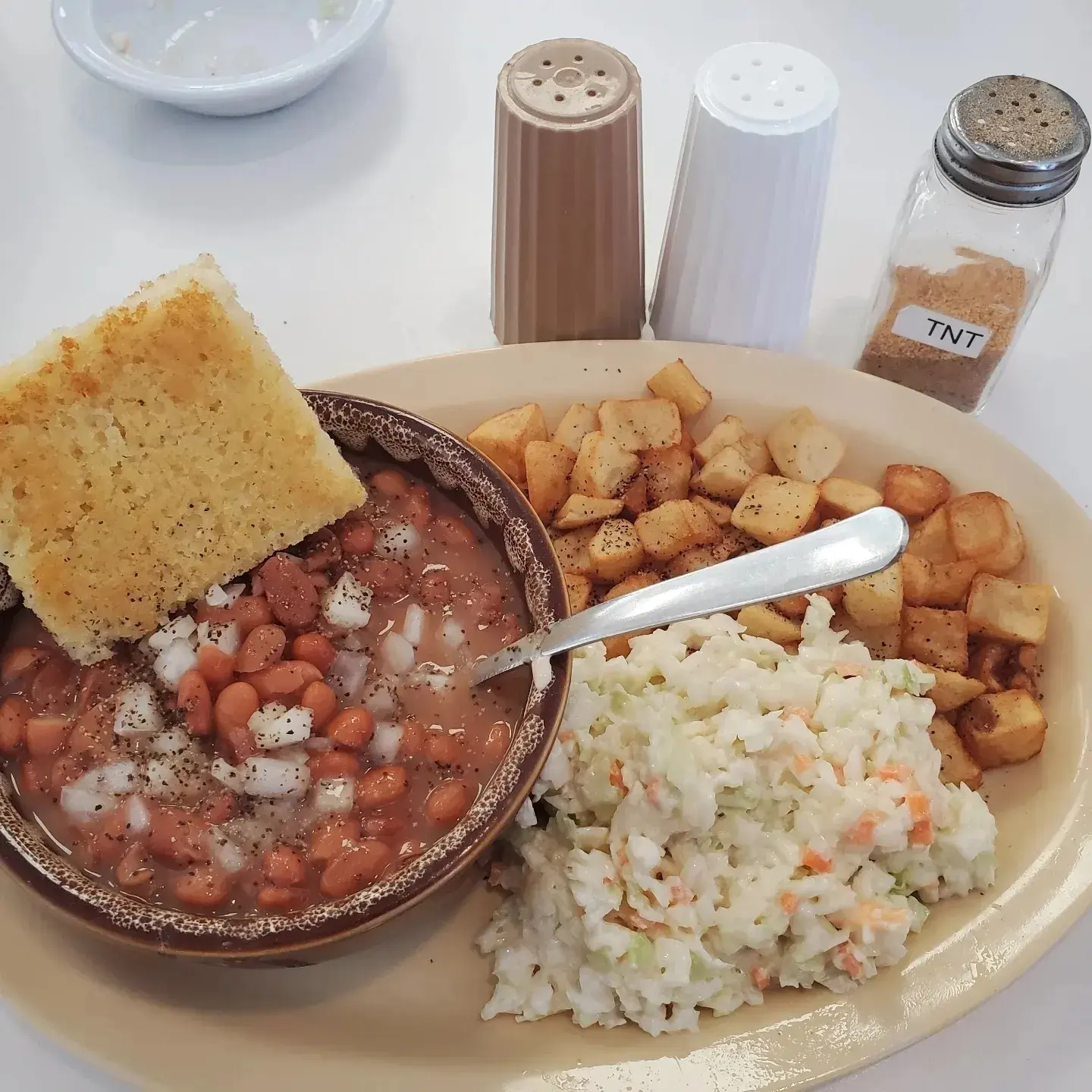 Beans, cornbread, coleslaw, and potatoes on plate.